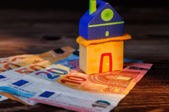 Wooden toy house on Euro banknotes on a dark table with natural sunlight for European housing market crisis and mortgage concepts.