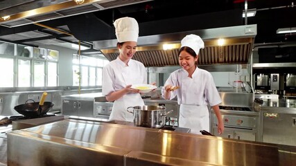 Two chefs in white uniforms and hats collaborate while cooking on a stove in a sleek, modern kitchen, showcasing culinary expertise, teamwork, and food preparation in a professional setting.