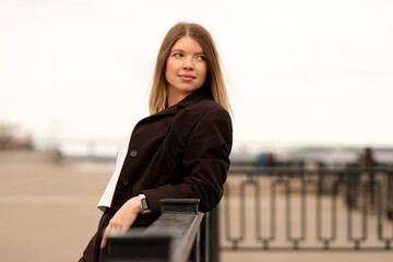 Woman in brown suit posing with hand in hair by waterfront. Natural feel with soft light. Casual, confident pose and expression add genuine and approachable vibe