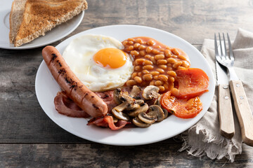 Full English breakfast with fried egg, bacon, sausages and beans on wooden table