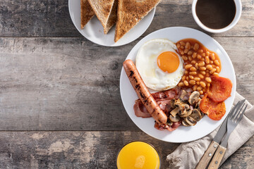 Full English breakfast with fried egg, bacon, sausages and beans on wooden table. Top view. Copy space