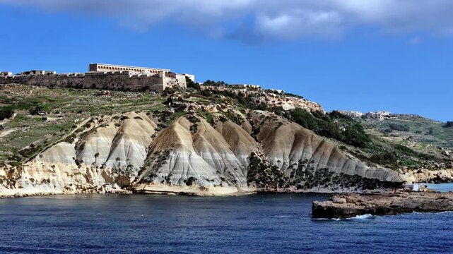 Aerial panorama of historic Fort Chambray bastions overlooking turquoise Mediterranean waters and unique blue clay cliff formations in Gozo Malta during a bright sunny summer day