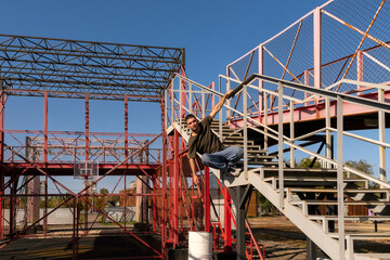 Man executes side vault over stairs in metal parkour structure. Freerunner performs a dynamic side vault using one arm to control movement over metal stairs in an outdoor urban training structure 
