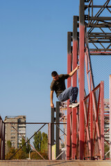 Freerunner descending red metal frame during parkour training. Male freerunner carefully descends a red metal structure during an outdoor parkour training session under a bright sky