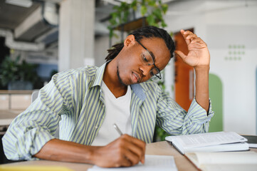 Focused university student taking notes and studying from textbook