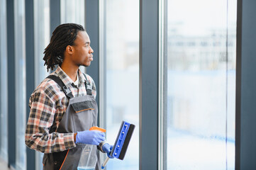 African American Professional cleaning service worker washing windows in office building