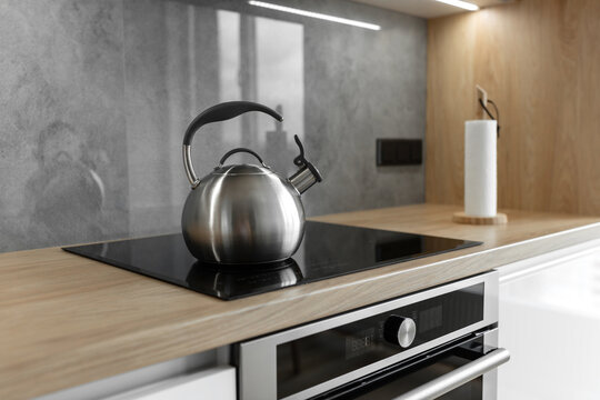 Photo of gray stainless steel kettle on the induction cooktop in the kitchen.