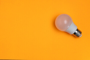 Minimalist photo of a light bulb against a bright orange background.