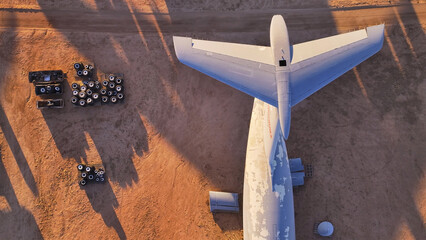 Aerial view of the tail of a retired aircraft casting long shadows on the desert floor, surrounded by discarded tires and vehicle parts, Tucson, Arizona, United States.