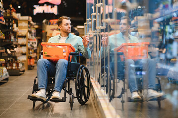 Obraz premium Customer using wheelchair choosing groceries in supermarket refrigerator section