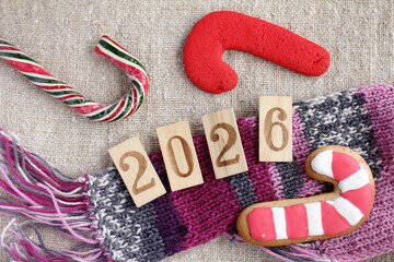 Number signs lie on a knitted scarf next to gingerbread cookies, top view. Happy New Year 2026