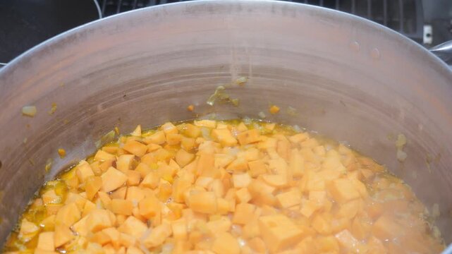 Close view of concass&eacute; cut yam, Dioscorea rotundata, gently saut&eacute;ing in fat inside a metal pot as a technical base for velout&eacute;, showing controlled cooking process, texture change, starch release