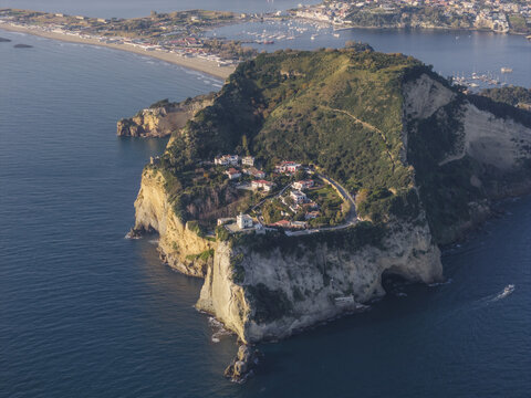Aerial view of the dramatic cliffs meet the turquoise sea, framing the quaint village nestled atop Capo Miseno, Bacoli, Campania, Italy.