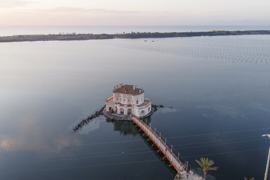 Aerial view of Casina Vanvitelliana's ornate architecture mirroring in the still waters, connected by a slender bridge, Fusaro Lake, Bacoli, Campania, Italy.