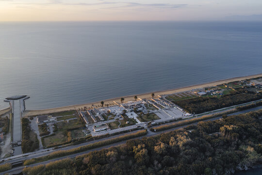 Aerial view of the tranquil lake meeting the sea, bisected by a strip of land dotted with buildings and lush trees under a soft, pastel sky, Fusaro Lake, Bacoli, Campania, Italy.