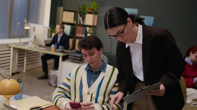 Handheld shot of adult female worker with clipboard rebuking young male employee for inconsistencies in report while working in office
