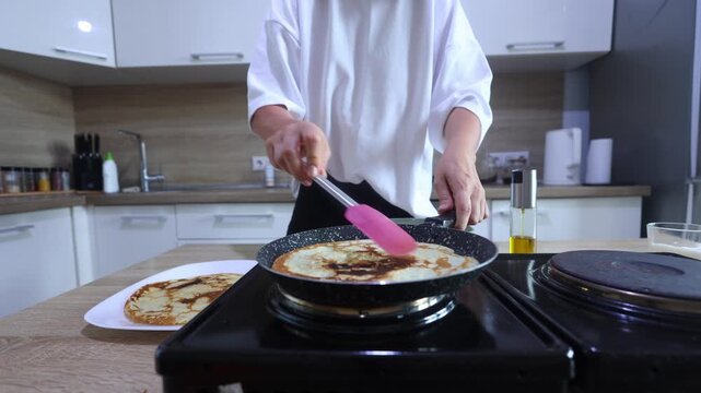 A person uses a pink spatula to expertly flip a pancake in a hot skillet. The pancake reveals a perfectly golden-brown cooked side as it lands back in the pan.