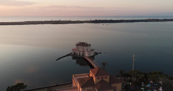 Aerial view of Casina Vanvitelliana's architecture reflecting in the still lake waters under the soft light of the sunset, Fusaro Lake, Bacoli, Italy.