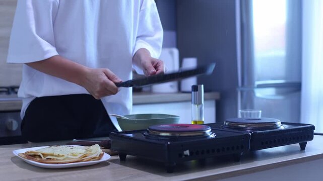 A cook demonstrates a flawless crepe flip using only a pan no spatula. The delicate batter cooks evenly, then lands perfectly on a plate with others. Great for home chefs mastering French breakfast cl