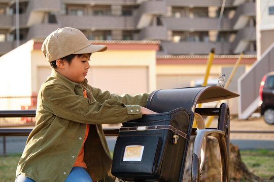 Japanese boy putting his belongings into a randoseru school backpack outdoors - Powered by Adobe