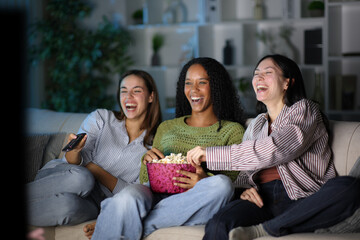 Happy diverse friends eating popcorn watching tv in the night