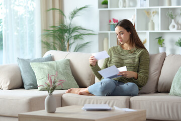 Fototapeta premium Serious woman in green reading a paper letter at home