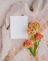 Elegant wedding card mockup with dried flowers and soft fabric backdrop set on a rustic textured surface