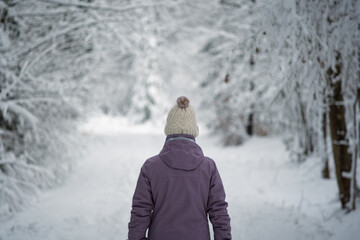Rear view of an unrecognizable young woman in winter active clothing walking through a snow covered forest. Close up shot, shallow depth of field, fresh snow cover on the tree branches