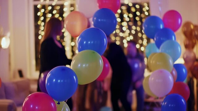 Colorful balloons fill a party room, with blurred figures dancing