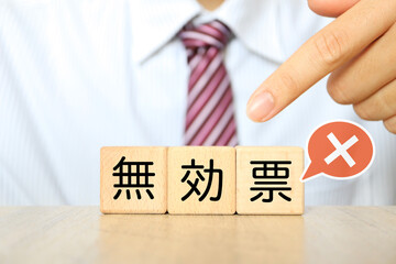 無効票を示す木製ブロックを持つ男性の手元。