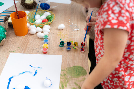 Little girl paints easter eggs at home for the spring holiday