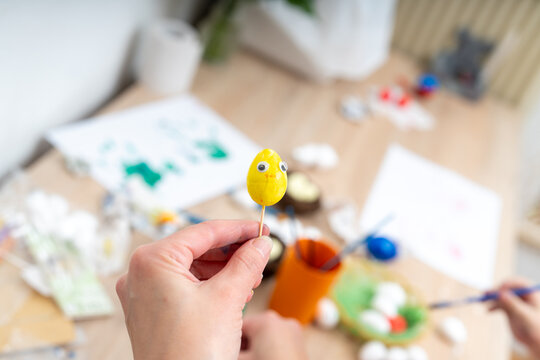Preparing for Easter person holds painted yellow egg with googly eyes on a stick - Powered by Adobe