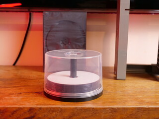 Stack of optical discs in clear plastic case standing on wooden surface under warm light.