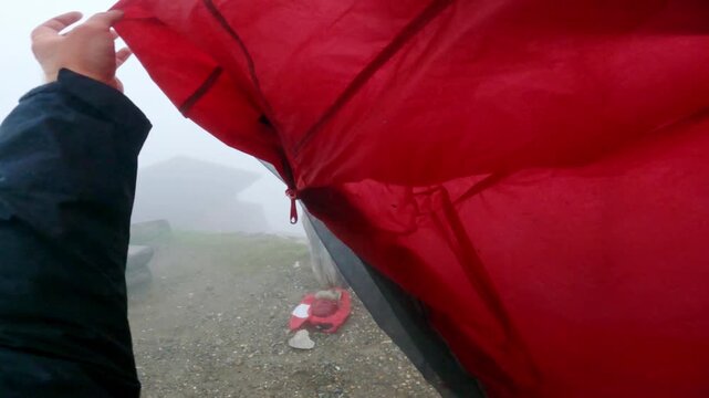 Misty cold morning as man folds wet camping tent alone outdoors in alpine region