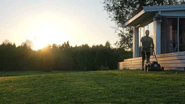 Man cutting lawn in a backlit sunset. Slow motion