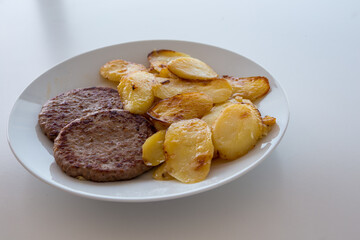 Hamburger con patate al forno su piatto bianco