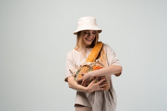 Happy young woman hugging reusable mesh grocery bag with fresh food, zero waste shopping and eco friendly lifestyle