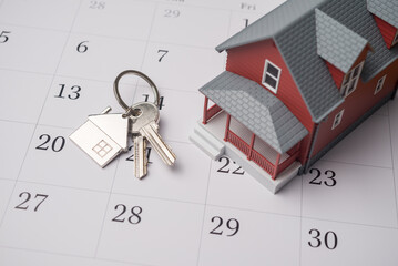 House model and key on white calendar background. Mortgage loan for buying home or real estate property, home finance, money saving planning, money risk management, installment schedule concept.