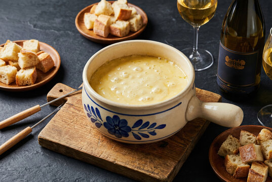 Traditional Swiss cheese fondue in a ceramic caquelon served with crusty bread cubes and white wine.