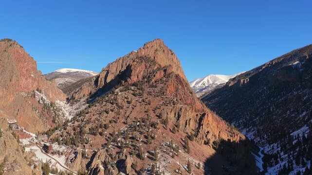 A cinematic aerial vista highlights a sharp, prominent mountain peak. Clear winter light and rugged rocky textures define the immense scale of this high-altitude mountain summit.
