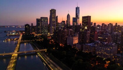 Obraz premium Aerial perspective of a metropolis skyline at dusk. Bright city lights illuminate tall buildings and structures with a colorful twilight sky
