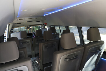 Interior view of empty minibus passenger cabin featuring rows of comfortable brown seat with headrest and blue ceiling lighting strip designed for comfortable travel and shuttle transportation