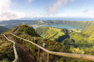A scenic view of a lake and mountains with a wooden fence leading to the top at Sete Cidades, Azores © Barosanu
