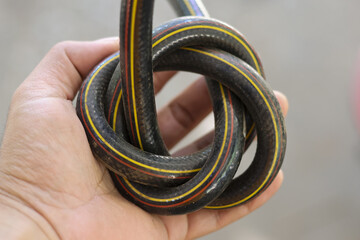 Close up hand holding knotted black rubber hose with yellow stripe showing concept of problem complication and tangled mess in abstract style on blur gray background