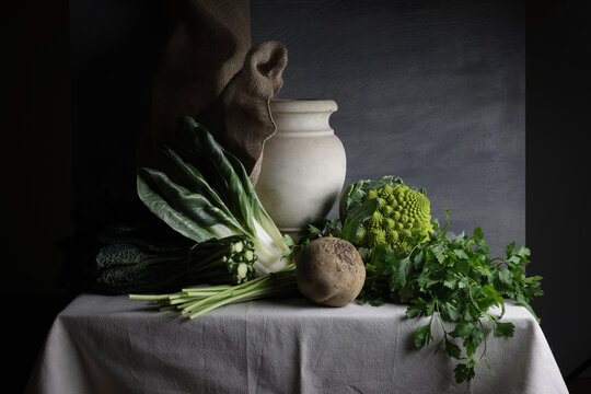 Composizione vegetale con vaso in marmo e ortaggi freschi su tavolo rustico
