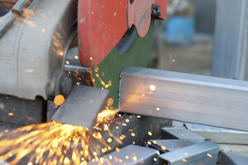 Close up industrial electric circular saw cutting steel pipe with bright sparks flying in busy...