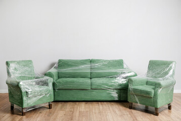 Green sofa and chairs wrapped in plastic in a simple room with wooden floor
