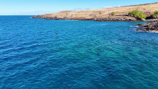 Aerial view of a person hydrofoil surfing over the clear, blue ocean waters under a bright sky, creating a mesmerizing scene, Hawi, Hawaii, United States.