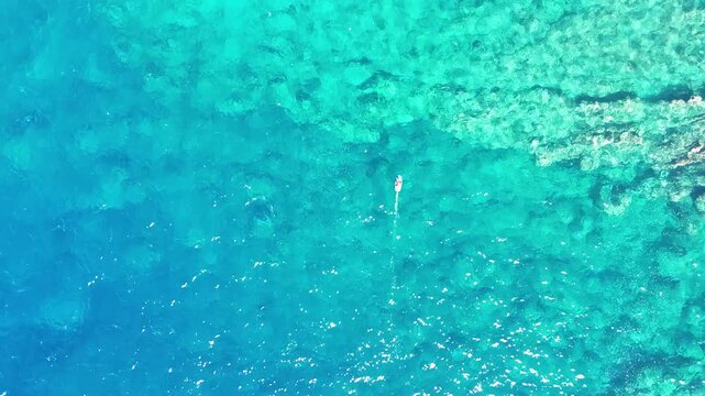 Aerial view of a person hydrofoil surfing over the clear, blue ocean waters under a bright sky, creating a mesmerizing scene, Hawi, Hawaii, United States.
