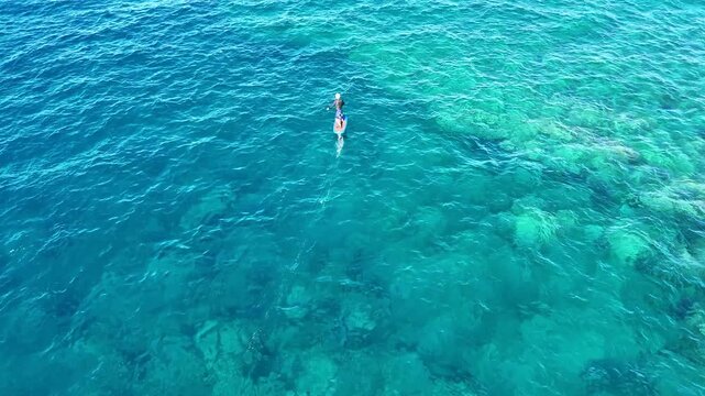 Aerial view of a person hydrofoil surfing over the clear, blue ocean waters under a bright sky, creating a mesmerizing scene, Hawi, Hawaii, United States.